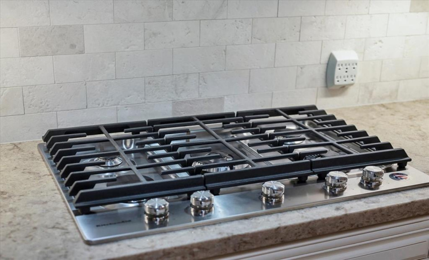 The backsplash in the kitchen features subway tiles which accent the high end appliances such as this six burner kitchenaid gas cooktop.