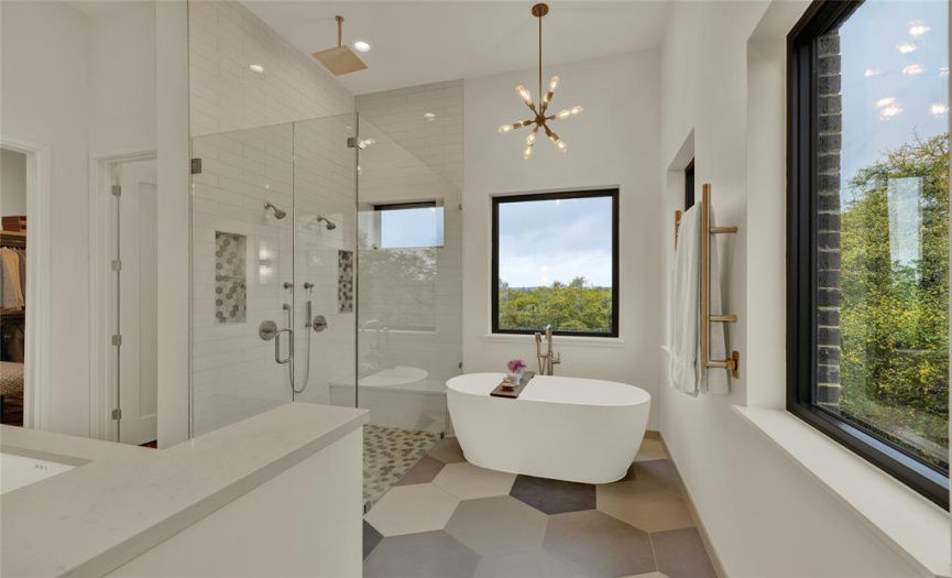Main bathroom with stand alone soaking tub, walk in shower, accent chandalier, and large octagon tiled floor.  Views of the Hill Country through the windows. 