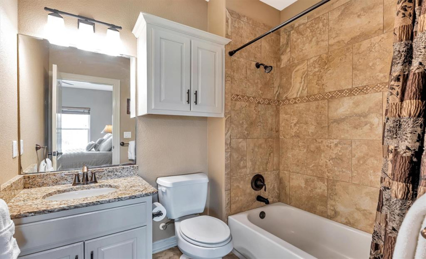 Attached bath to Bedroom 2 with granite counters, antique bronze accents, tile flooring, tile tub surround with decorative accent band and linen cabinet.
