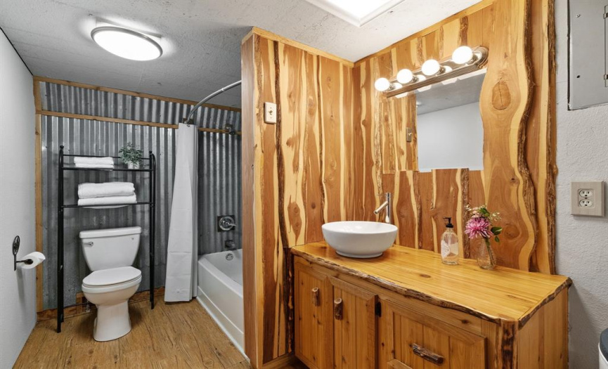 The full bathroom is sure to impress with naturally carved, knotty wood cabinetry and accent wall, raised bowl sink, stylish fixtures and hardware, shower/tub combo, and metal accent wall.