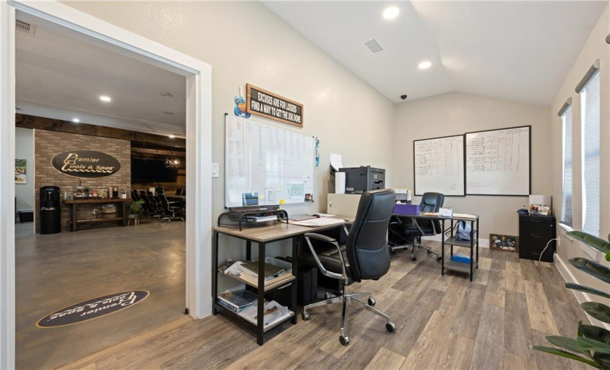 Behind the white barn door, there is another large office space with room for three desks, wood-look tile flooring