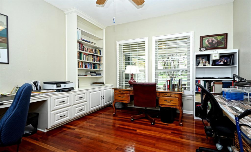 Dual glass doors open to a wood floor front office with wall built-in's and plantation shutters.