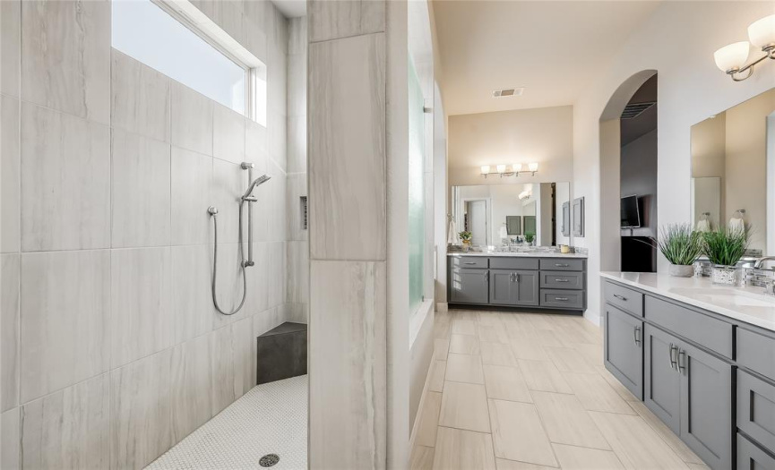 Neutral tile encases the walk-in shower, complete with natural light, a corner bench, and penny tile floors.