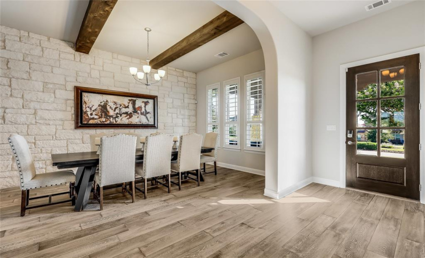 As you step inside, you'll be greeted by a bright aesthetic, guiding you past a formal dining room with a captivating stone wall backdrop and beamed ceilings.