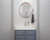 Darling half bath on main level featuring designer mirror, shiplap wall, and pretty powder blue/lavender cabinetry.  