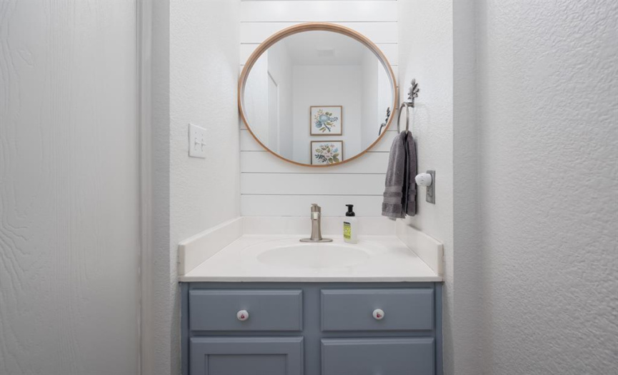 Darling half bath on main level featuring designer mirror, shiplap wall, and pretty powder blue/lavender cabinetry.  