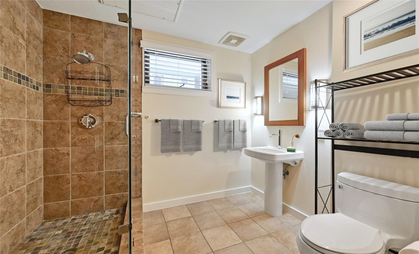 *Virtually Staged* Discover the stylish second bathroom featuring a sink, mirror, tasteful tiles, fresh paint, a frameless shower, a small window for natural light, a well-placed light fixture, and convenient bath towel poles.