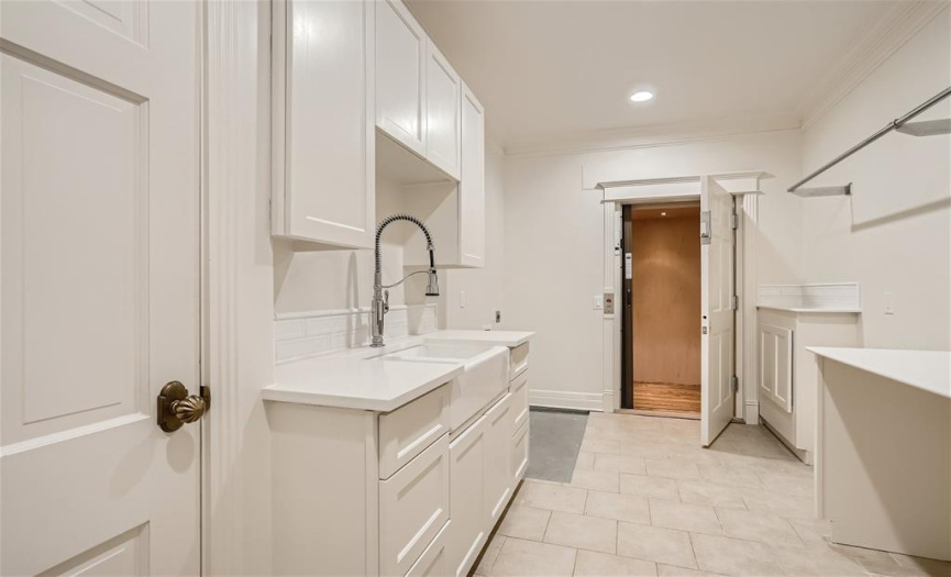 Large utility room with a farm house sink, space for two washing machines, and an elevator that goes from the corner of the kitchen to this utility area