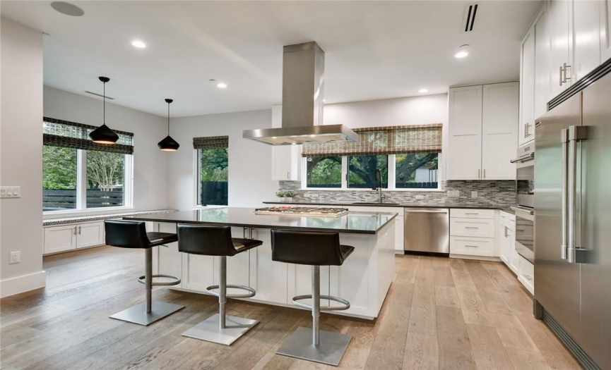 Incredibly well-equipped kitchen with built-in refrigerator & freezer, double ovens, island with gas cooktop & exhaust hood, tile backsplash, plenty of storage, bar & casual dining seating options. 