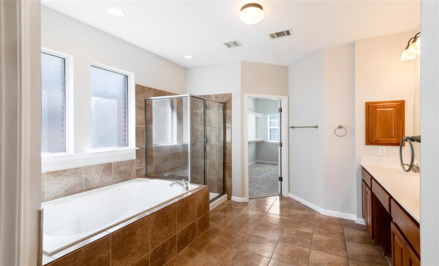 Master bath includes a vanity with two sinks, a garden tub with tile surround, separate shower with tile surround, tile flooring, and a water closet.