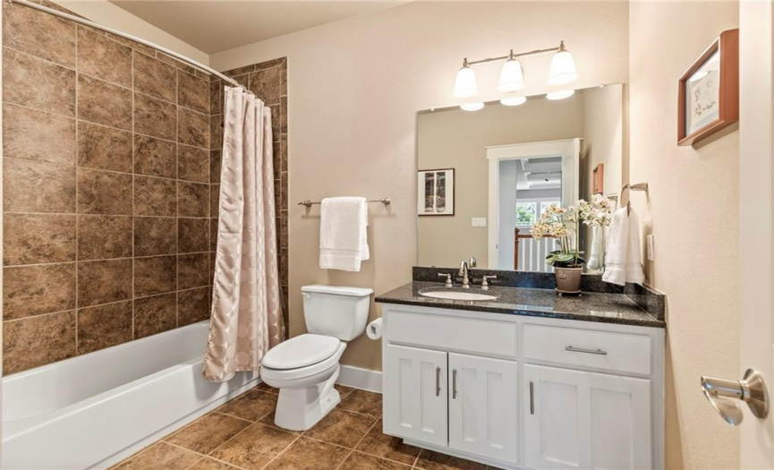 The shared guest bathroom has a large single vanity with ample storage space and a tub/shower combo with tile surround.