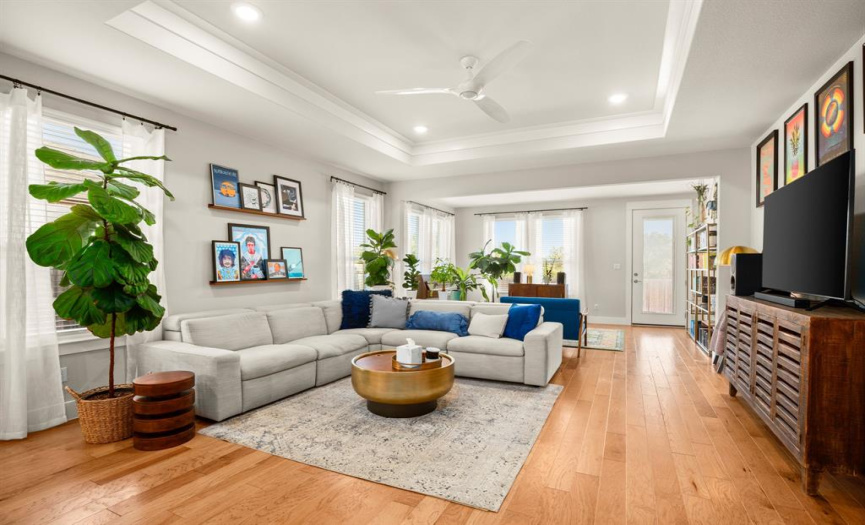 The spacious living room is enhanced with a tray ceiling, crown molding, and a modern ceiling fan for additional comfort during the summer months.