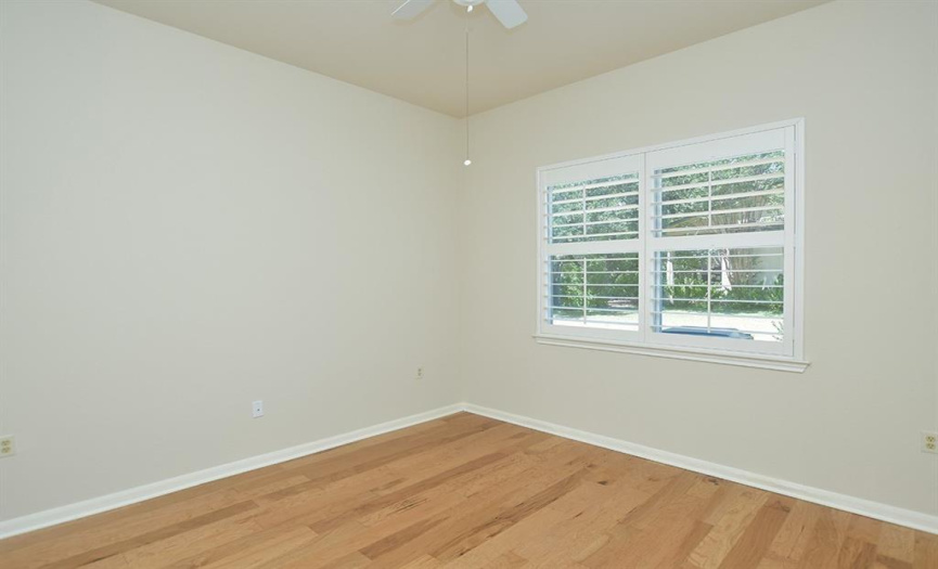 The guest bedroom looks to the side of the home through a double shuttered window.