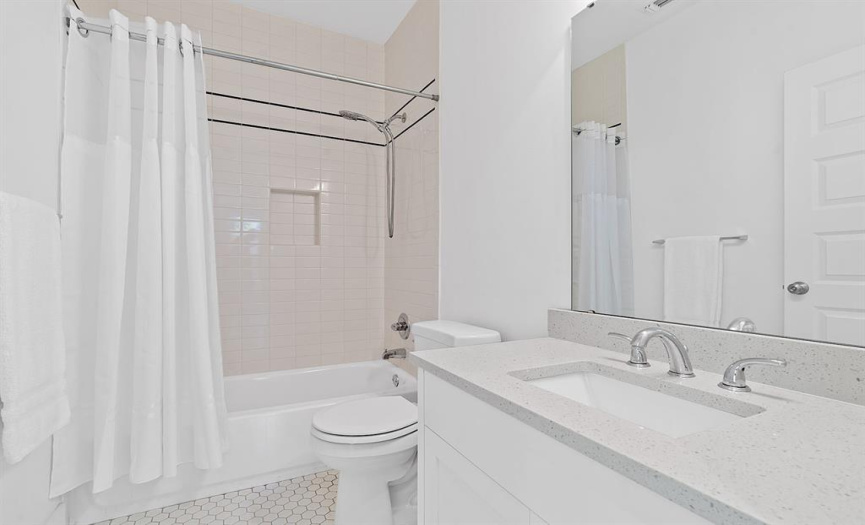 Another full bathroom features tiled flooring and shower, and a quartz vanity countertop.