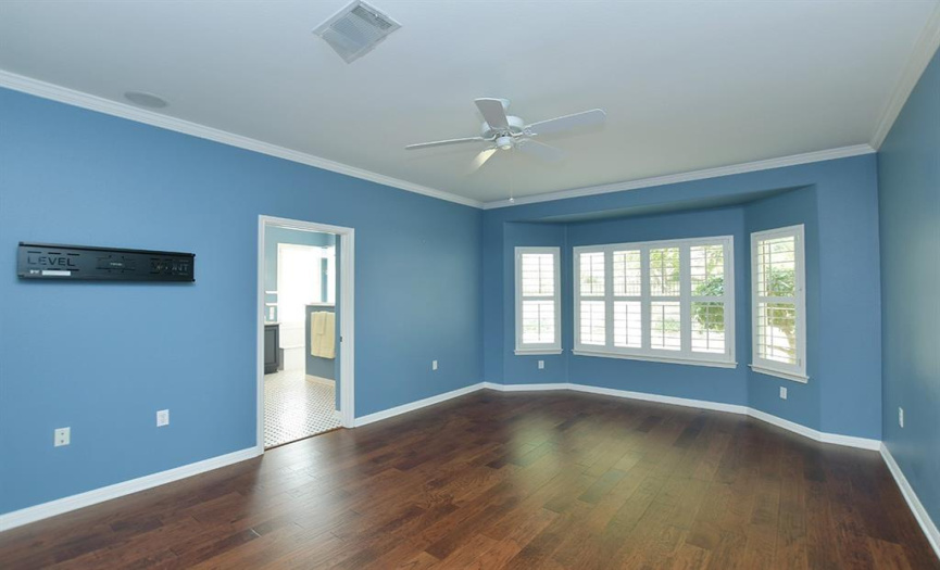 Wood floors, plantation shutters and crown molding provide the basis for your decorating choices in this primary bedroom.  A bay window looks to the pretty fenced backyard.