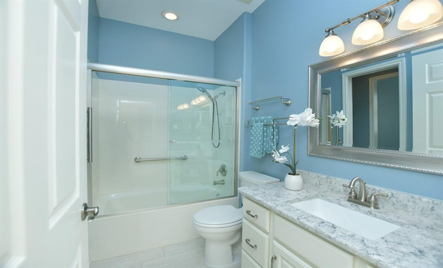 The guest bathroom is mere steps from the guest bedroom and has been updated with comfort height toilet, quartz counter tops, designer mirror, painted cabinetry and light floors tiles in the same brick pattern found in the rest of the home.
