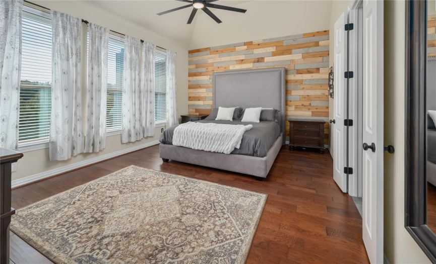 Primary bedroom with designer wood accent wall, hardwood flooring, and exceptional hill country views