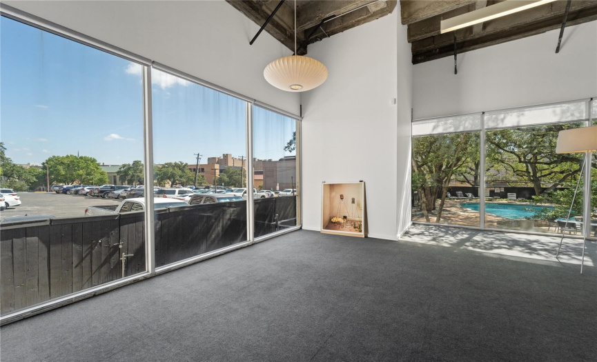 This open floor plan office space, nestled on the first floor of a stylish condo building, showcases a seamless blend of contemporary design and functionality. Large windows, adorned with elegant curtains, let in an abundance of natural light, creating a welcoming and airy environment.