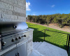 Propane grill in outdoor kitchen down to backyard with greenbelt behind