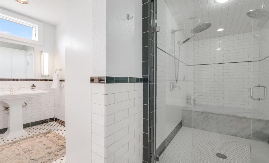 There is an oversized walk in shower with floor to ceiling subway tile and multiple shower heads