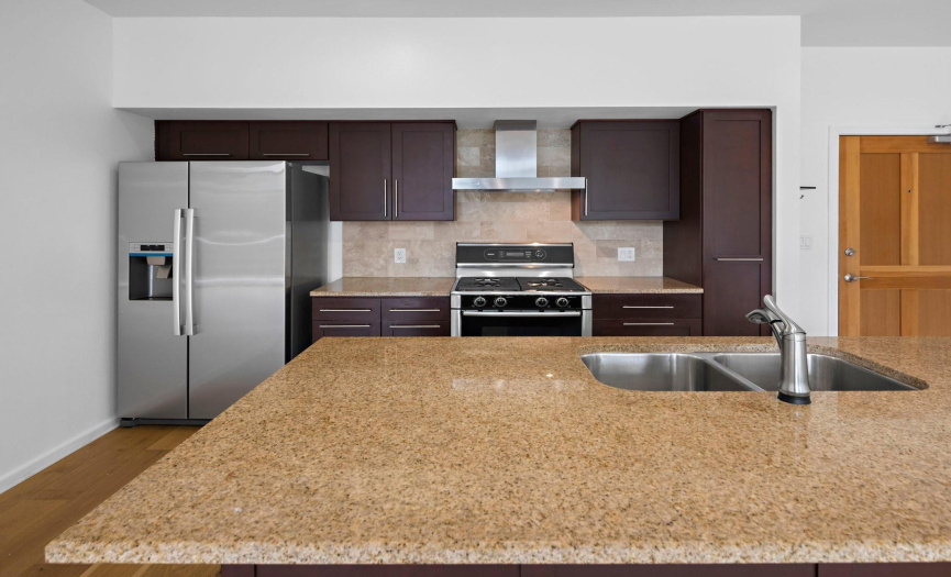 The meticulously crafted kitchen boasts stainless steel appliances, granite countertops, tile backsplash, wood cabinetry, and a center island with bar seating