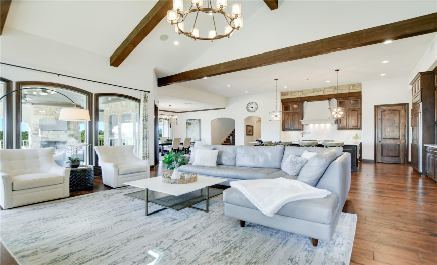 The expansive living area boasts undeniable elegance and comfort, with a vaulted, wood beamed ceiling, a sparkling chandelier, and flawless finishes that abound throughout.