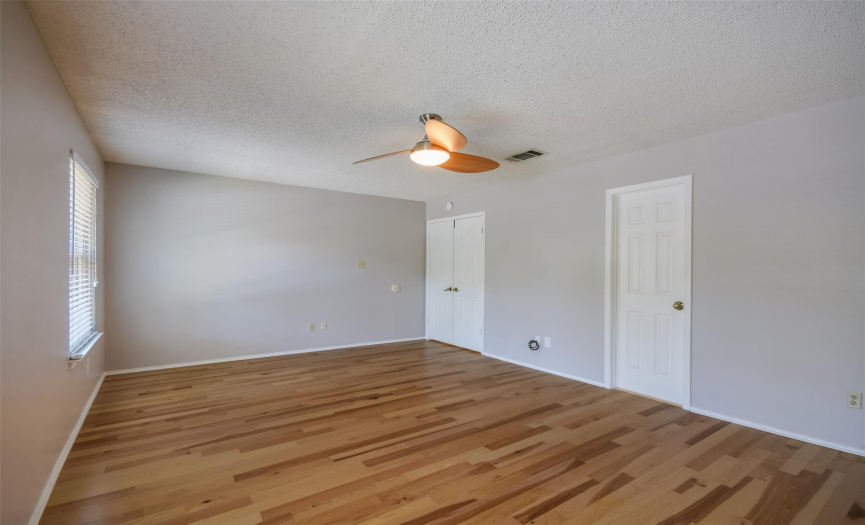 primary bedroom w/ updated ceiling fan, real wood flooring, walk in closet and attached full bath