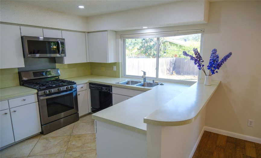Open kitchen with LG stove, microwave & refrigerator and large window over looking back yard.  Cabinets freshly painted.