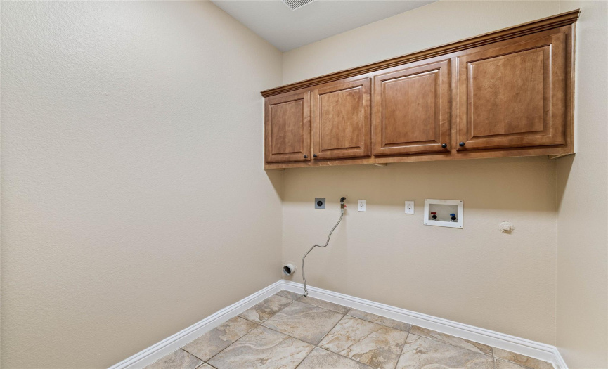 Spacious utility room with upper cabinets and electrical and gas outlets for dryer.