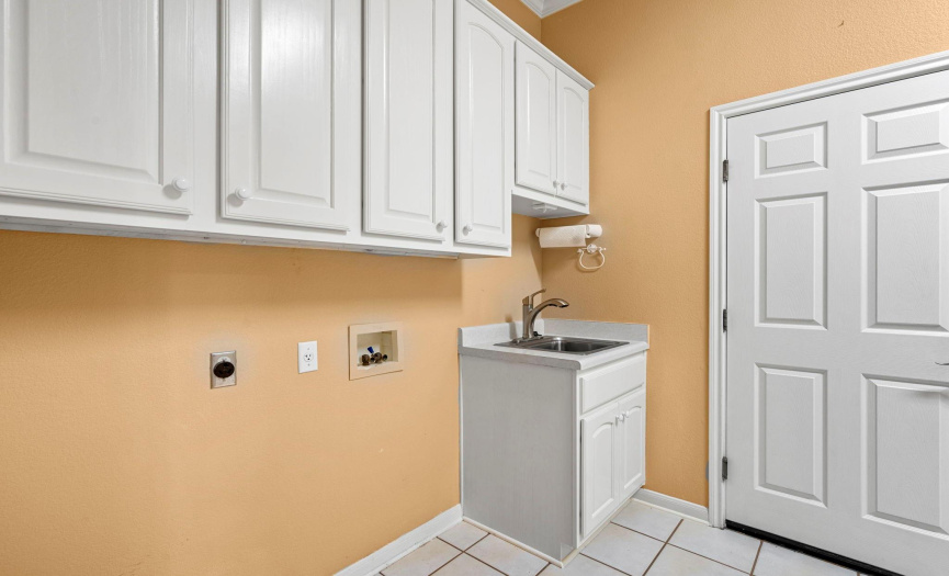 The laundry room is well equipped with cabinets, a sink, and a bonus area.