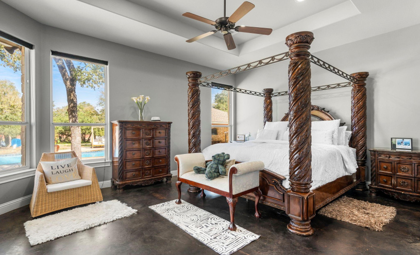 Primary suite with tiered ceiling and large picture windows that overlook the backyard resort.  