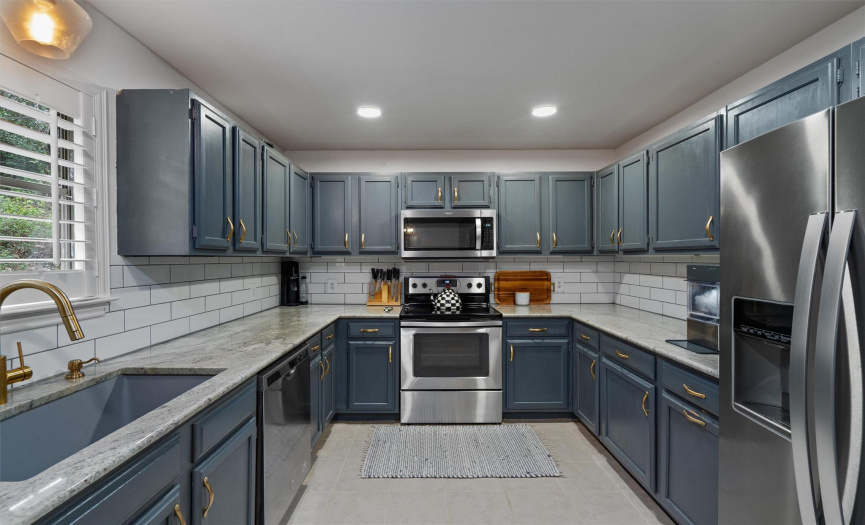 A full kitchen renovation includes granite countertops, a farmhouse sink, recessed lighting, decorative backsplash, painted cabinetry, and stylish hardware. 