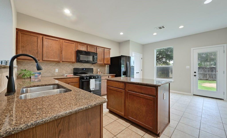 Spacious kitchen with island, granite counters, upgraded faucet and black appliances.