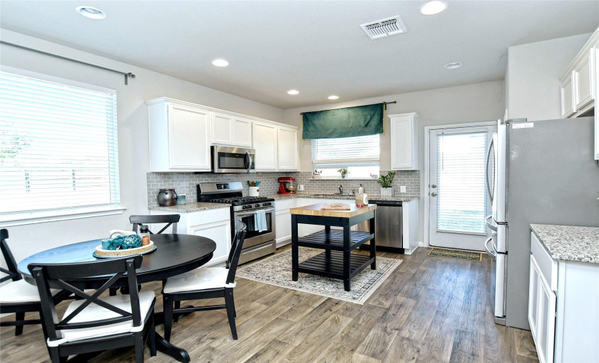 Modern well laid out kitchen with stainless steel appliances, granite counters, glass subway tile, and plenty of storage next to dining area.