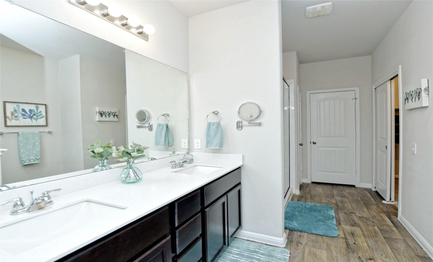 En-suite primary bathroom has dual vanities, lots of cabinet space, very large walk-in shower, toilet with bidet, and great walk-in closet.   The door at the back is an oversized linen closet with room for additional storage in front of the shelves.