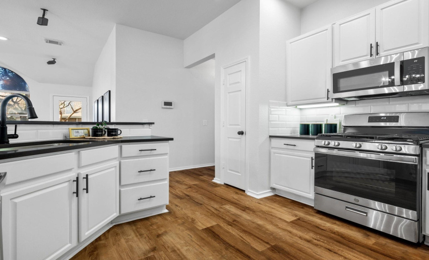 The recently remodeled kitchen is a showstopper, featuring white cabinetry with new black matte hardware, a new faucet, quartz countertops, a tile backsplash, and stainless appliances