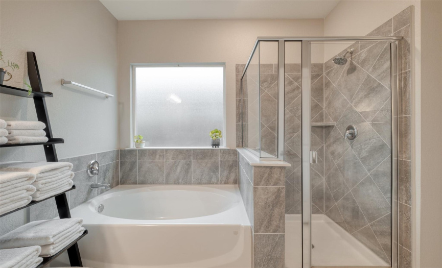 The ensuite showcases a relaxing soaking tub and a separate walk-in shower, both enveloped by neutral tile.