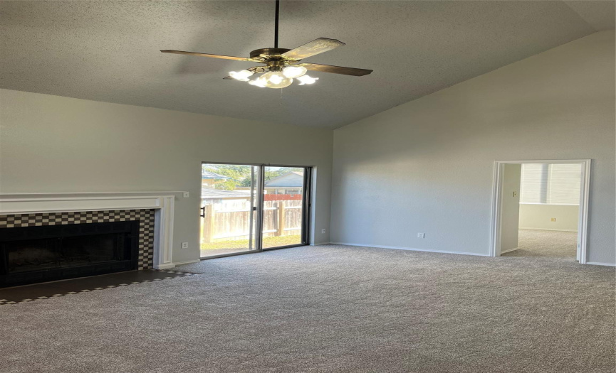 Spacious main living room with fireplace, ceiling fan, clean carpets & high ceiling.