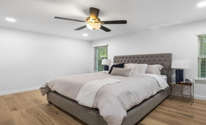 The primary bedroom is graciously-proportioned with wood flooring, a ceiling fan, and LED recessed lighting.
