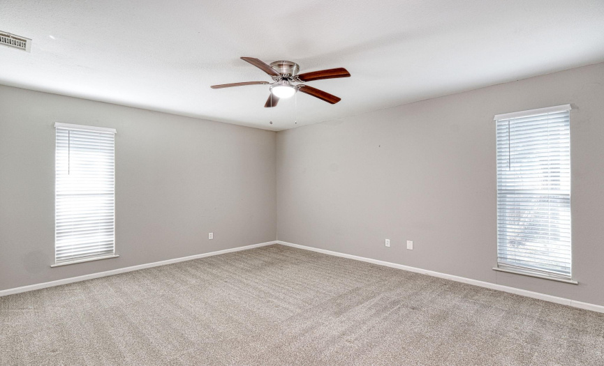 The primary bedroom has a ceiling fan and two large windows that allow for natural light and carpet throughout.