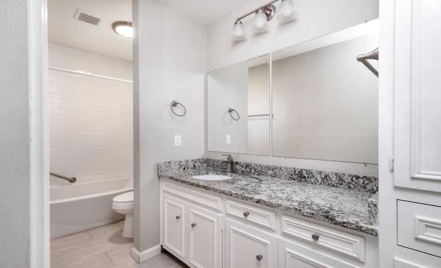 The primary bathroom has tile throughout, a tub/shower combo, and large granite single sink vanity. 