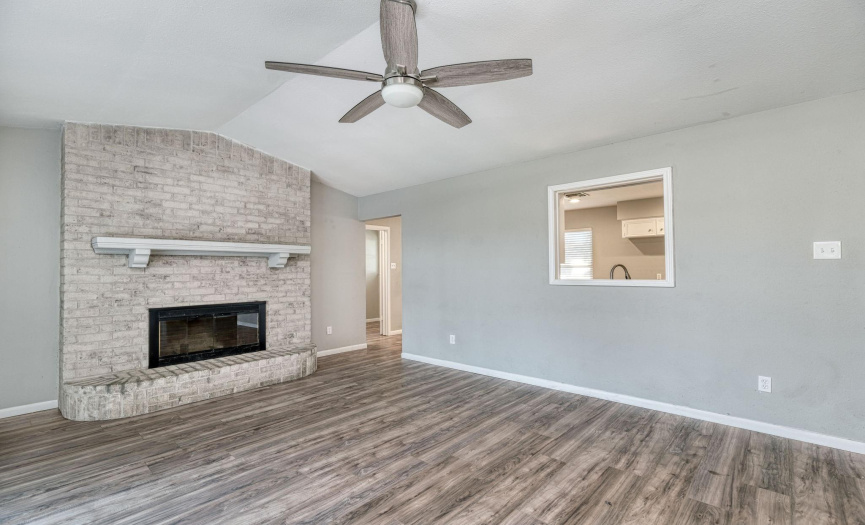 The living room has a brick wood burning fireplace and vinyl plank flooring throughout. The living room connects to a dining area and the kitchen. 