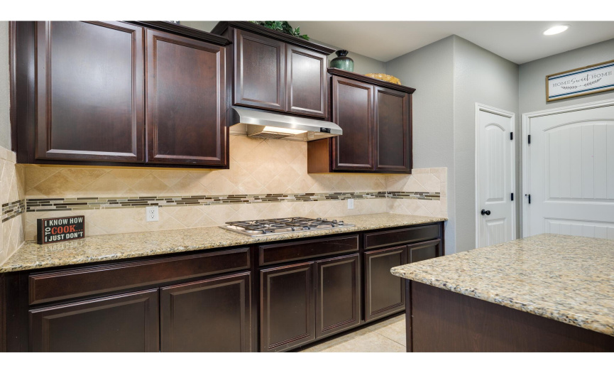 A built-in gas range rests below the range hood, while granite counters and tile backsplash nicely complement each other.