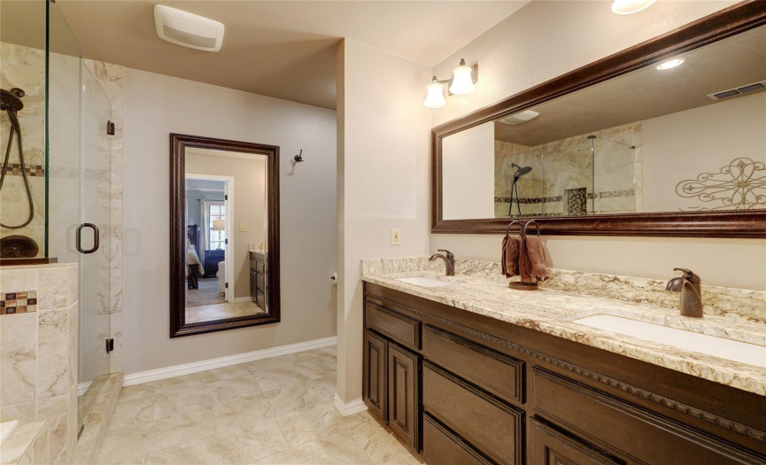 Remodeled primary bathroom with gorgeous granite, dual sinks, framed mirror, updated lighting, walk-in shower, and soaking tub.