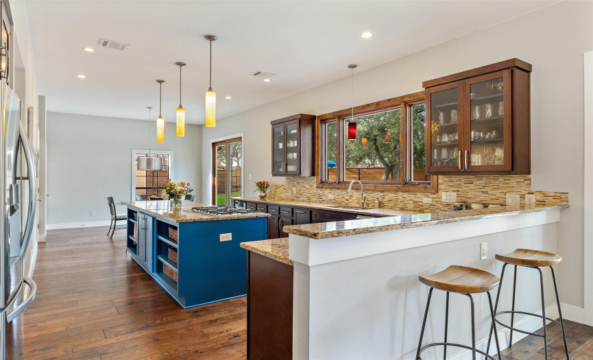 Cook in an airy and open kitchen with natural light and views of the backyard pool area. Guests can keep the cook company when preparing meals on the gas cooktop in the center of the kitchen.