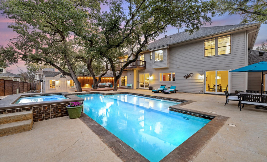 In the backyard, a sparkling pool and inviting spa with lush trees with wooden fencing around the property for privacy. 
