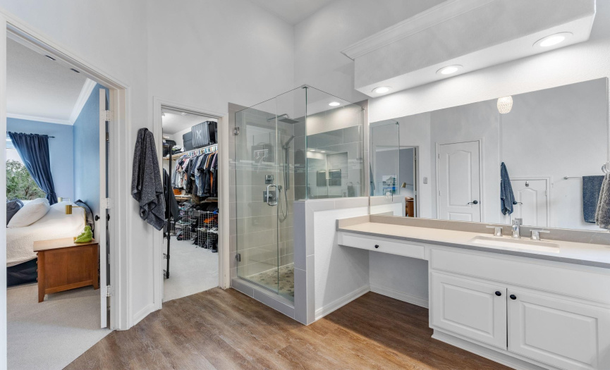 The master bath has an updated shower, garden tub, two vanities with updated counters, vinyl plank flooring, water closet, storage closet, and Duet-style blinds on the window.