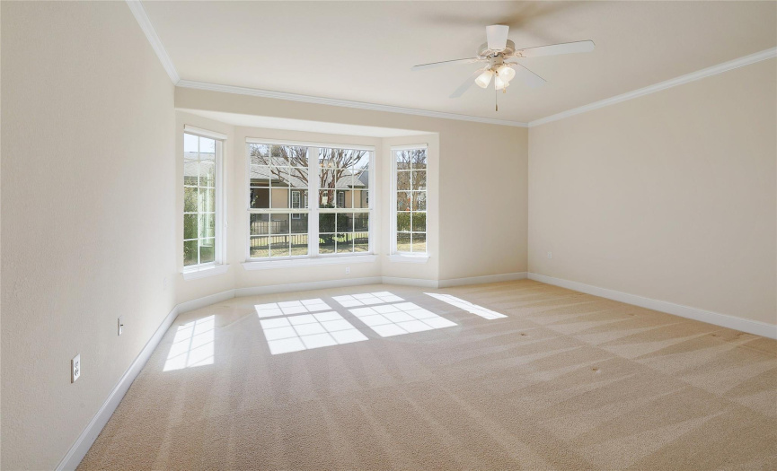 Main bedroom is comfortably carpeted with a bay window and crown molding.