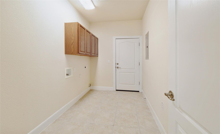 A lengthy laundry room with upper cabinets.
