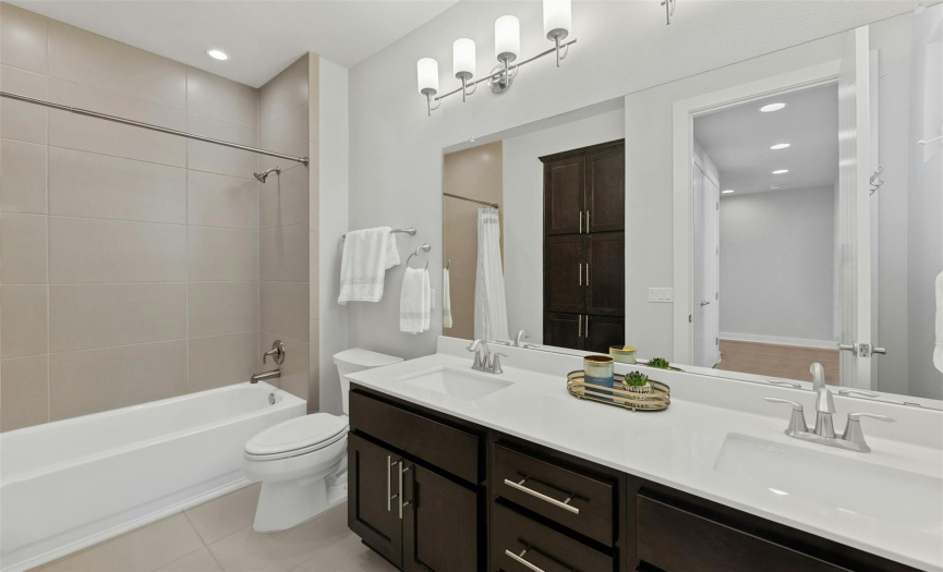 This beautiful full guest bathroom provides a spacious dual vanity, a shower/tub combo with tile backsplash, and built-in linen storage. 